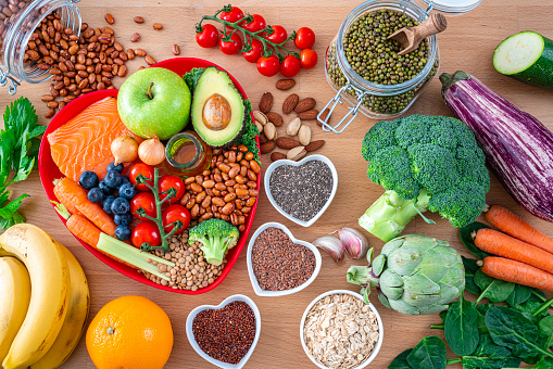 Heart care concept. Overhead view of a group of food that contains healthy nutrients for heart care shot on wooden table. The composition includes extra virgin olive oil, legumes, avocado, berries, nuts and seeds, salmon, broccoli, carrot, soy beans, brown lentils, eggplent, spinach, oats, artichoke, apple, tomato, garlic among others. High resolution 42Mp studio digital capture taken with SONY A7rII and Zeiss Batis 40mm F2.0 CF lens