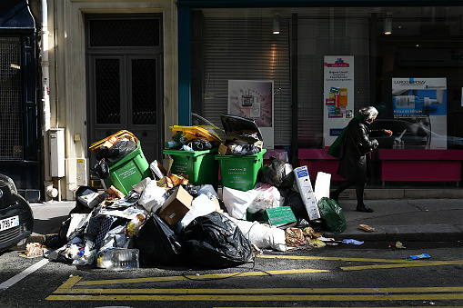Paris, France-03 15 2023: A person passing next to a pile of waste and garbage cans that overflows in a street in Paris, because of the garbage collectors' strike