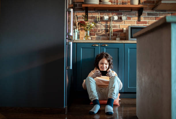 istock Young boy using  his smart phone while sitting on the floor in the kitchen 1473675904