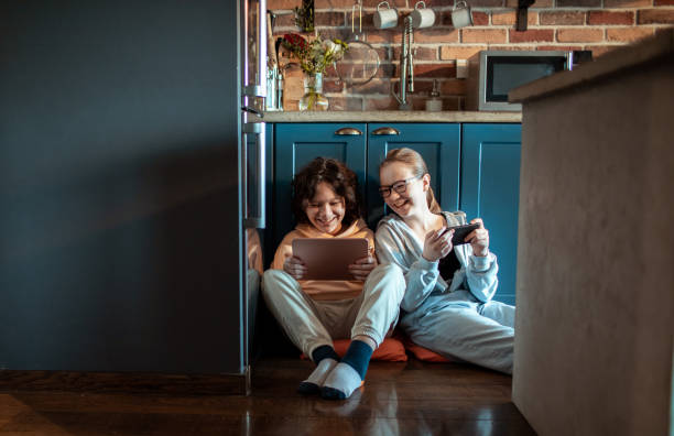Young brother and sister using their mobile devices in the kitchen