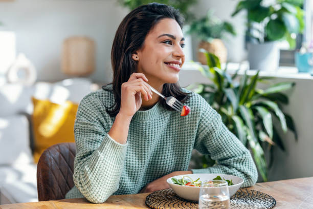 bella donna sorridente che mangia insalata sana a casa. - strawberry fruit food food and drink foto e immagini stock