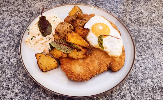 turkey schnitzel, fried egg, coleslaw, and potatoes on white plate