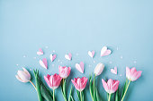 Pink tulip flowers and paper hearts on blue table. Spring floral arrangement for Mothers day.