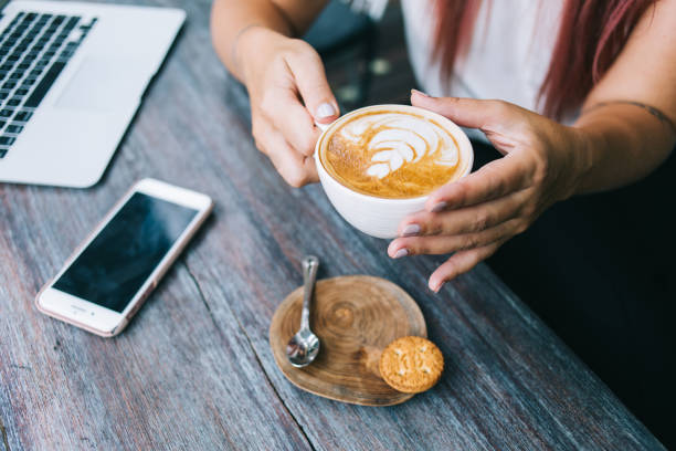 istock Crop lady drinking coffee with cookie after freelance work on laptop 1473687792