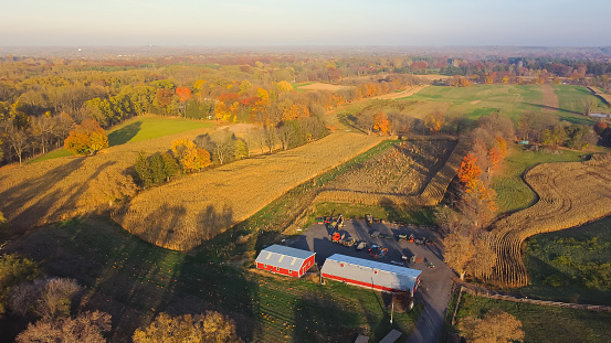 Aerial view scenic fall season in countryside of Rochester, Upstate New York, rolling corn field to horizonal line, traditional red barn, farming equipment. Scenery small American town autumn leaves