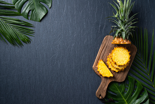 Top view of fresh cut pineapple with tropical leaves on dark blue background.