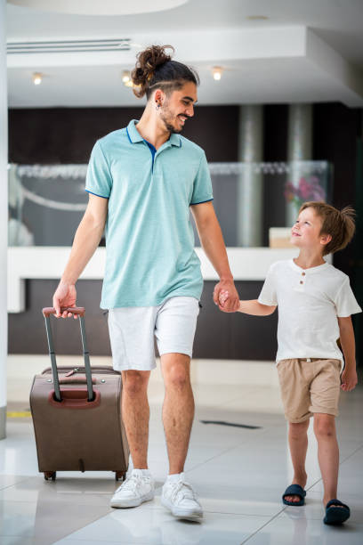 istock Father and son holding hands and walking in hotel lobby 1473689356