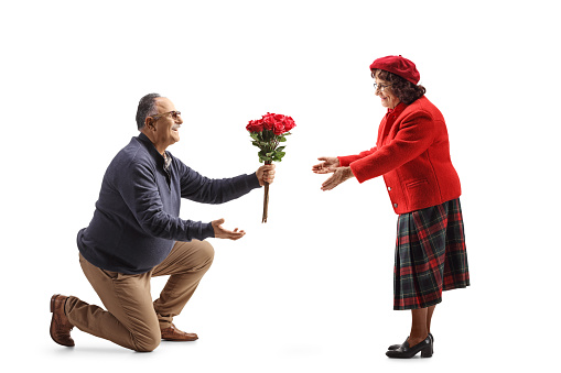 Mature man kneeling and giving a bunch of red roses to a woman isolated on white background