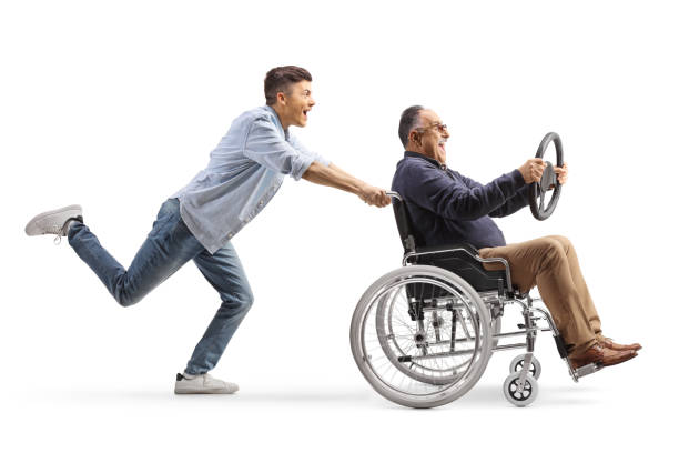 full length profile shot of a guy pushing a mature man in a wheelchair holding a steering wheel - physical injury men orthopedic equipment isolated on white imagens e fotografias de stock