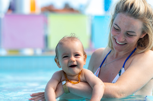 Happy mother and baby girl enjoying in the pool during summer day
