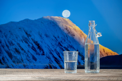 Bottle of pure water and a glass on a wooden table with the snowy Himalayan mountains background and full moon , close up