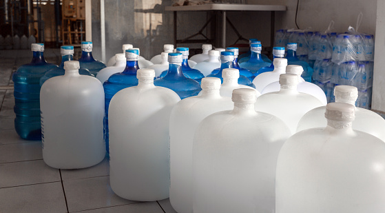 Plastic big bottles or white and blue gallons of purified drinking water inside the production line. Water drink factory