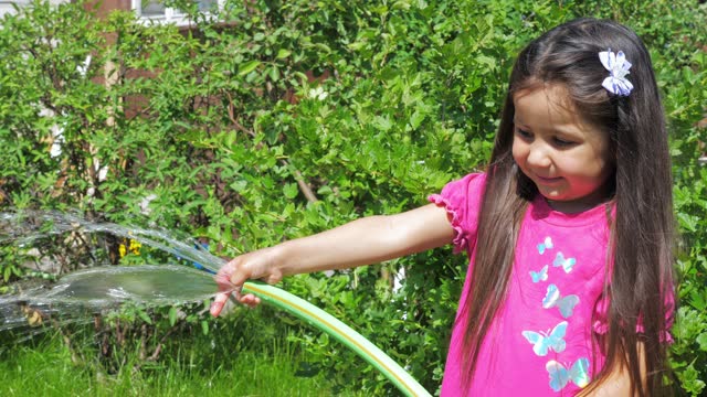 Little cute girl holds a watering hose in her hands