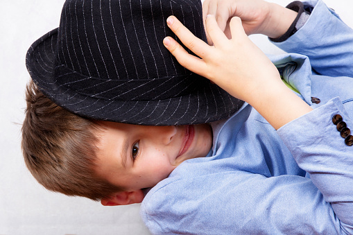 The boy half covered his face with a hat and smiles. Children's secrets.