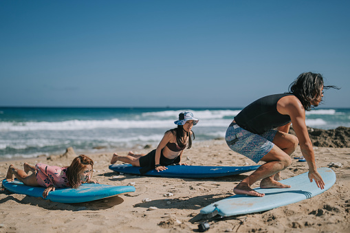 Asian Chinese wave surfing male instructor guiding female students at beach before surfing in sea