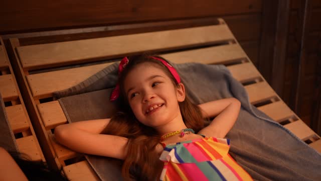A little girl rests on a wooden deck chair