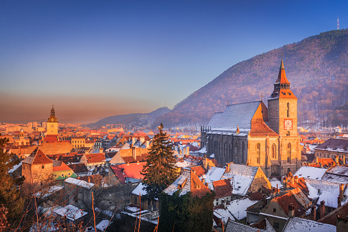 Brasov, Romania. Winter snowy sunset with Black Church and Carpathian Mountains, winter travel in Transylvania.
