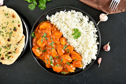Indian chicken curry with rice on plate over dark stone background. Top view, flat lay