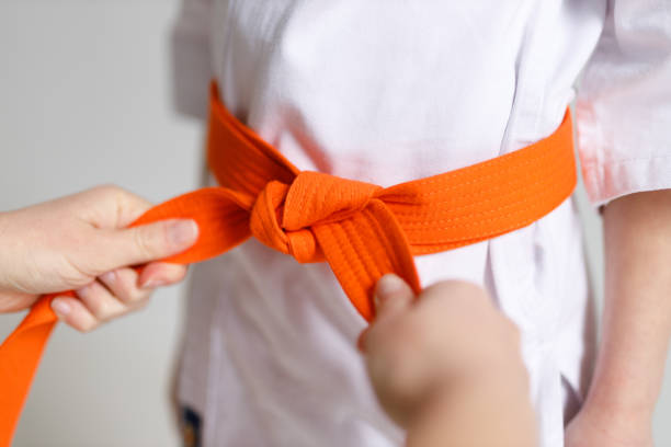 istock An adult's hands tie an orange karate belt on a child's kimono. 1473706380
