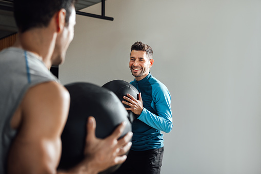 Smiling caucasian personal trainer holding medicine ball in a fitness class at the gym. Coach looking at Man doing workout. Horizontal, copy space.