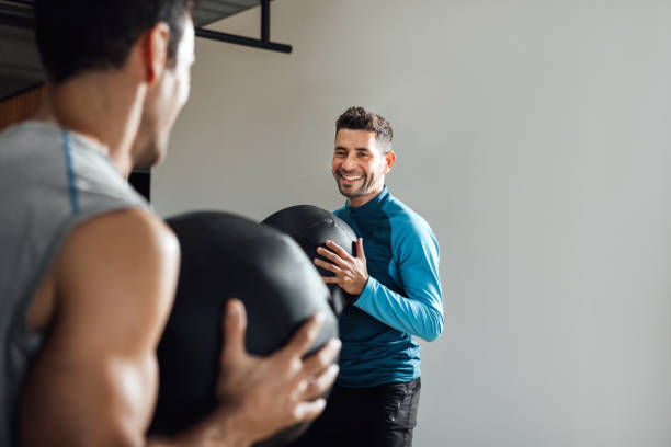 Smiling personal trainer in fitness class with medicine ball Smiling caucasian personal trainer holding medicine ball in a fitness class at the gym. Coach looking at Man doing workout. Horizontal, copy space. fitness trainer stock pictures, royalty-free photos & images