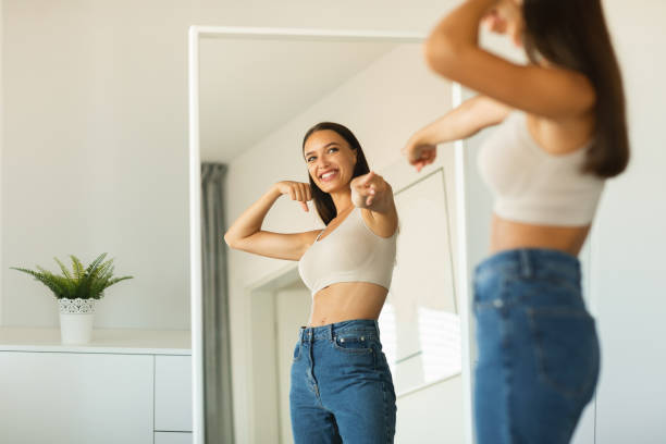 dama alegre señalando su reflejo en el espejo en casa - dieting mirror healthy lifestyle women fotografías e imágenes de stock