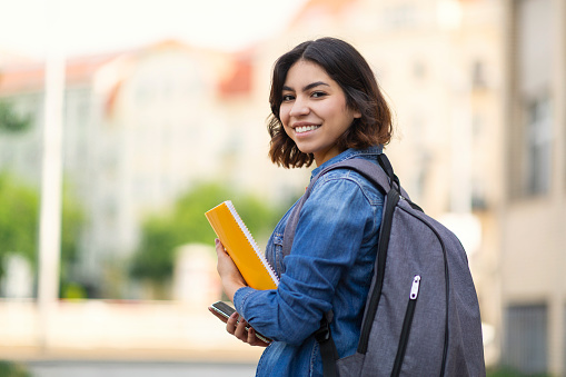 Smiling Young Arab Female Student With Workbooks And Backpack Standing Outdoors