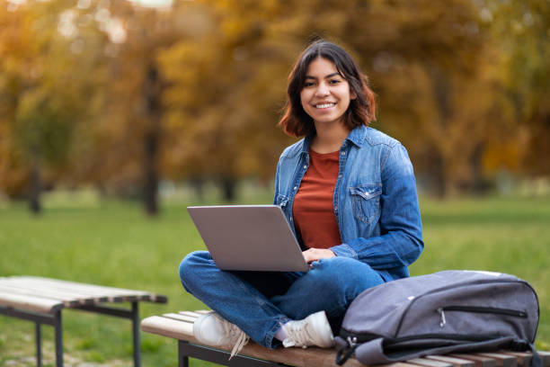 istock Middle Eastern Female Student With Laptop On Laps Sitting On Bench Outdoors 1473707816
