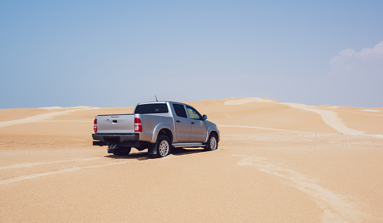 Big pickup truck of silver color parked on sand in desert and tire tracks after driving on sunny day during summer holidays