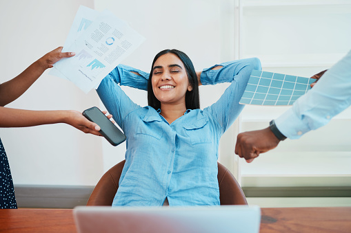 Young South Asian woman relaxes in office chair while coworkers make demands. High quality photo