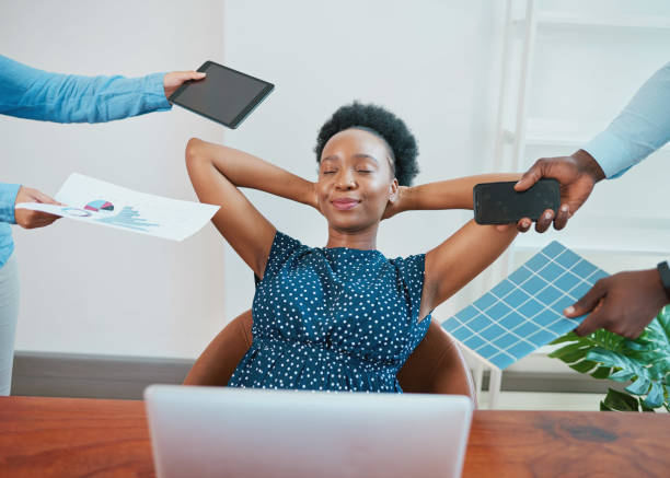 Young Black woman relaxes in her office while coworkers make demands stock photo