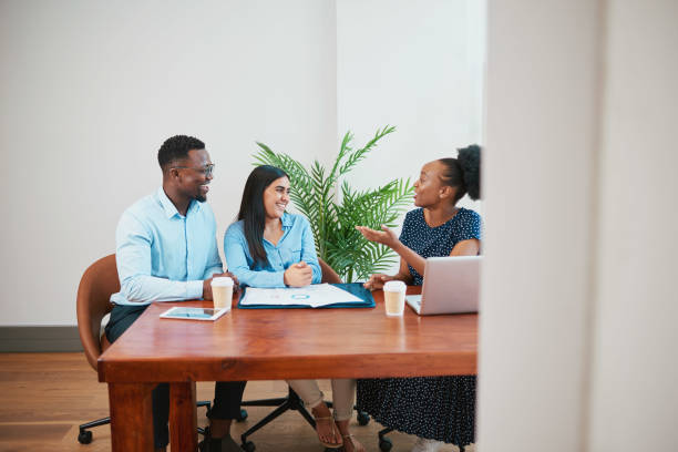 Wide shot of three business coworkers around boardroom table talking