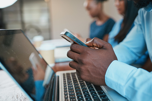 Close up of Black man's hands using phone during meeting, with laptop. High quality photo