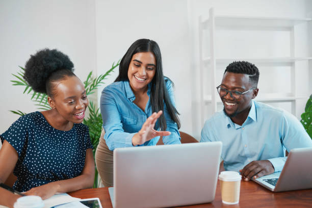 istock Three smiling business colleagues look at laptop in office while gesturing 1473709580