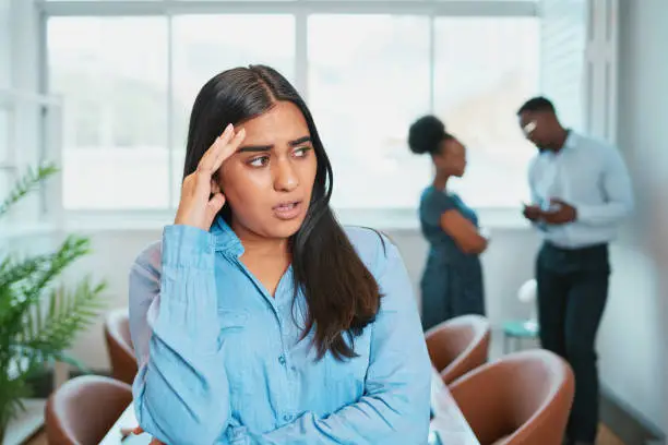 Photo of Young woman looks upset while colleagues talk behind her back, office drama