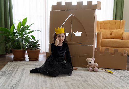 Cute little girl dressed up as a princess while playing with handmade castle