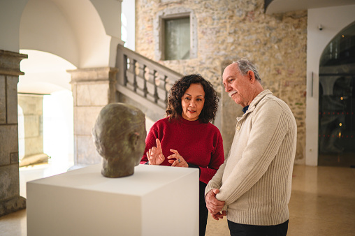 Waist up image of a beautiful mature  woman and her attractive  Caucasian male friend, standing in front of an exhibit and observing it while discussing something. Looking away.