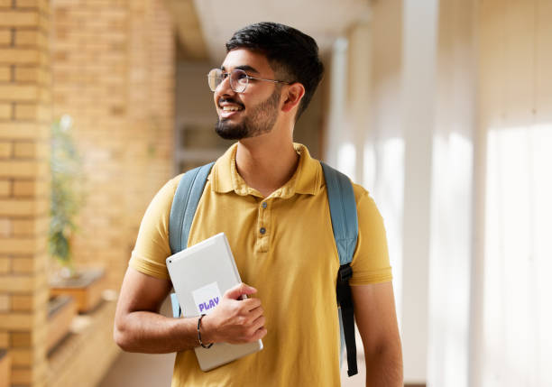 istock University student, college and indian man with a tablet and backpack while walking down campus corridor. Young gen z male happy about education, learning and future after studying at school building 1473711049