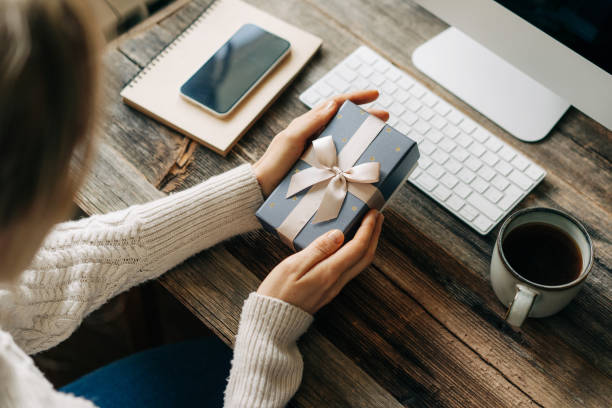istock Unrecognizable woman holding a gift box while sitting at a working office desk. 1473712167
