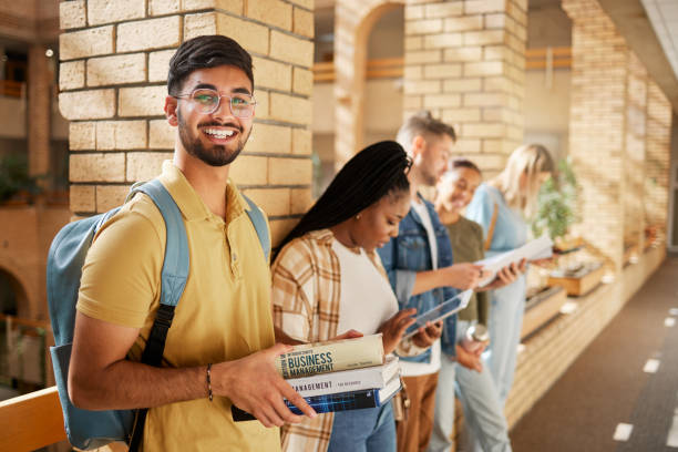 uniwersytet, korytarz i portret hindusa i studentów stojących w rzędzie wraz z książkami w szkole biznesu. przyjaciele, edukacja i przyszłość, szczęśliwy człowiek w grupie studyjnej na kampusie w holu na egzaminie - lecture hall university student seminar zdjęcia i obrazy z banku zdjęć