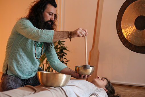 Mature man playing a rin gong during a sound massage therapy to a young woman.