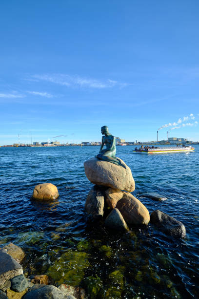 statua della sirenetta a copenaghen con barca turistica e inceneritore sullo sfondo - denmark danish culture copenhagen sculpture foto e immagini stock