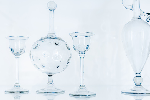 Transparent empty glasses and decanters over light blue background. Abstract glass installation