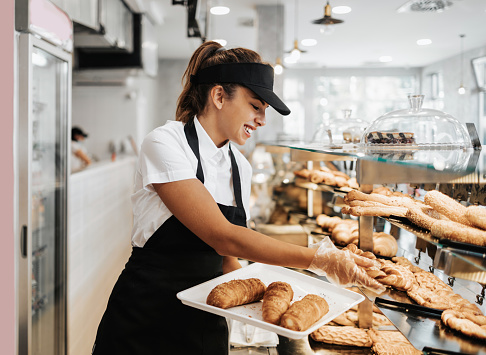 Beautiful young and happy female worker working in a modern bakery.