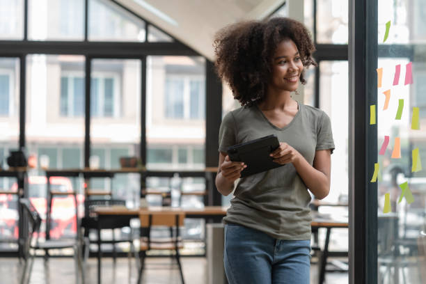 istock Young smiley attractive, businesswoman using sticky notes on a glass wall to write a strategic business plan to develop and grow to success. 1473717586