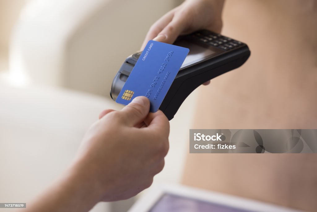 Hand of bank cardholder paying bill in cafe Hand of bank cardholder paying bill in cafe, applying blue credit card with chip at wireless payment terminal held by waitress, using electronic transaction banking technology. Clopped shot, close up Credit Card Stock Photo
