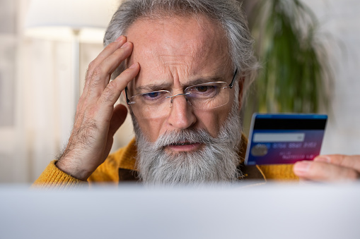 Upset senior man holding credit card. Online scam concept.