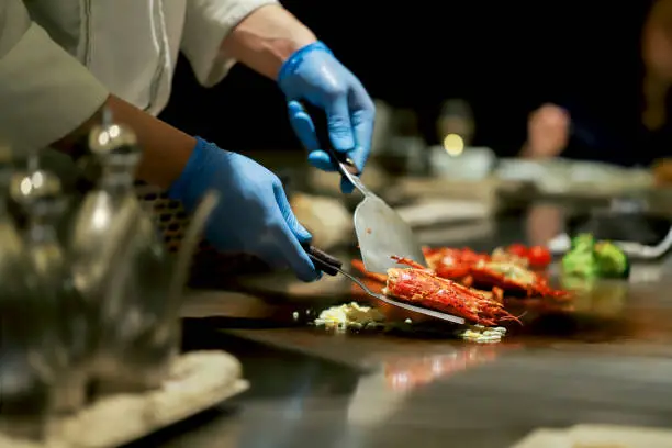 Teppanyaki chef cooks lobster dinner for guests wearing gloves for sanitation.