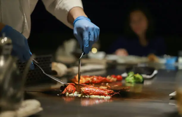 Teppanyaki chef cooks lobster dinner for guests wearing gloves for sanitation.