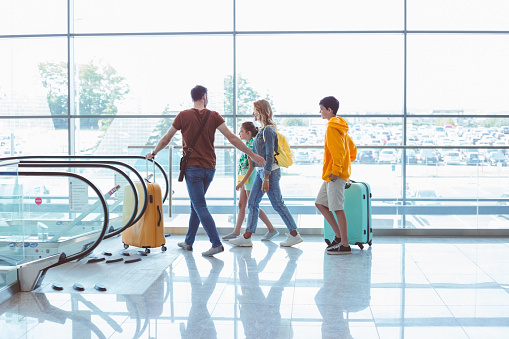 Side view of family with luggage walking at airport terminal, using escalator.